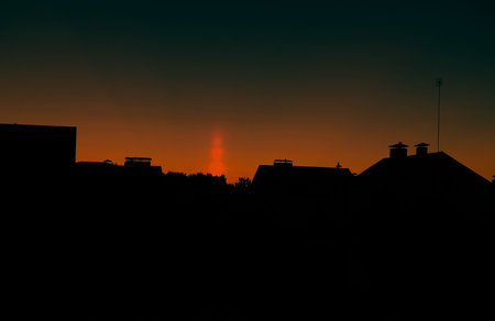a natural phenomenon of a light column. visual atmospheric phenomenon, optical effect, sunlight refracting in the air at sunset beautiful sunset sky over the roofs of houses.banner,poster.dramatic skyの写真素材