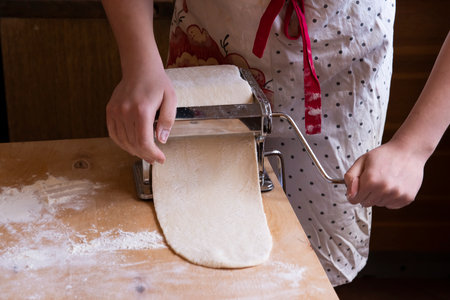 The girl rolls out the dough using a Pasta dough rolling machine.Automation of the process of working with the test at home.Spholyatella at home.the concept of technology in the confectionery Businessの写真素材