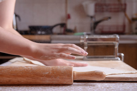 An interesting perspective on the process of making Italian pasta at home. Beautiful hands sprinkle flour and smooth the dough on the table at home. Cook at home. real people. atmospheric photoの写真素材