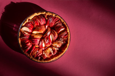 An open apple pie on a bright crimson background in the rays of the bright sun. Color 2023 Viva Magenta. Fragrant autumn pastries. attractive advertising.the delicious aroma of red apples wafts aroundの写真素材