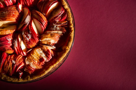 An open apple pie on a bright crimson background in the rays of the bright sun close-up. Color 2023 Viva Magenta. attractive advertising, copy space. the delicious aroma of red apples wafts aroundの写真素材