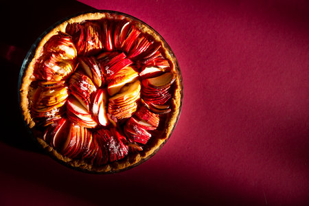 An open apple pie on a bright crimson background in the rays of the bright sun close-up. Color 2023 Viva Magenta. attractive advertising, copy space. the concept of holidays, prosperity and generosityの写真素材