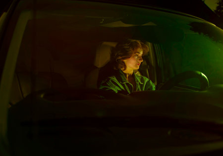 Portrait of a beautiful girl through the windshield of a car close-up. The car is illuminated by neon lights of city streets. conceptual photography of night travel, night life. insurance companiesの写真素材