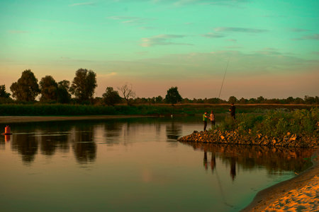 Beautiful river bank. the setting sun illuminates with warm rays a family that casts fishing rods on the shore. fishing. amazing landscape. the concept of a family vacation in nature. copy spaceの写真素材
