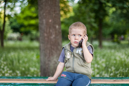 Little boy talking on the phone, listening, sitting outdoors,の写真素材