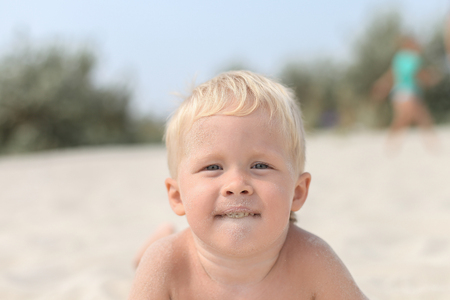 Little boy on the beach playing dirty in the sand, sand on the face, teeth, mouth,の写真素材