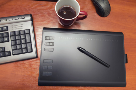 Graphics tablet with a pencil, part of the notebook and cup of coffee on a black wooden table, close up. Graphic tablet, keyboard, table, coffee, pen.の写真素材
