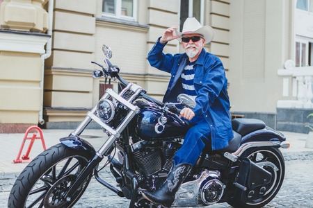 An elderly man in a cowboy hat is sitting on a motorcycle. A man on a motorcycle, wearing a cowboy hat.の写真素材