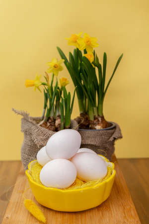 Vase with jonquil flowers, Easter eggs in basket and decor on shelf near wall