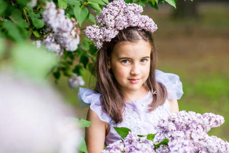 Beautiful little girl in dress with Lilac bouquet in garden. Spring blossom.の写真素材