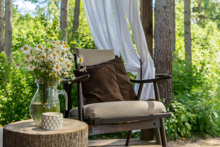 Wicker chair with basket, cozy beige pillow and flowers vase at a cafe terrace in a summer eveningの写真素材