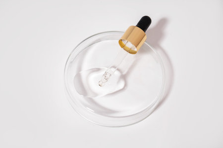 Drop falls from a pipette into a cosmetic bottle, isolated on white background