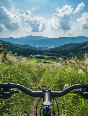 Mountain landscape from cyclist perspective. Peaceful countryside with rolling hills and green grass. Majestic mountains rise in distance. Perfect scenery for travel agency and tours.の素材