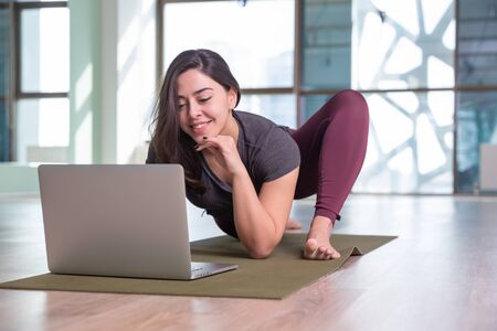 Photo of young woman practicing yoga with laptop indoor. Beautiful girl practice yoga in class. Yoga studio instructor. Blurred backgroundの写真素材