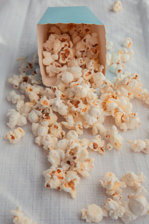 Fresh popcorn spilled out of the blue cardboard cups on a white surface Cinema snack concept. The food for watching a movie and entertainment.の写真素材