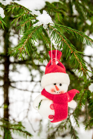 Toy snowman hanging on a snow-covered treeの写真素材