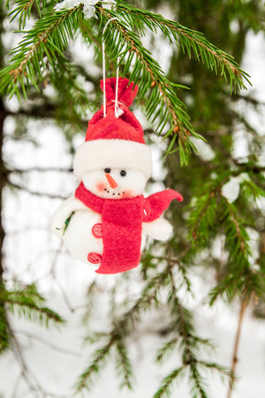 Toy snowman hanging on a snow-covered treeの写真素材