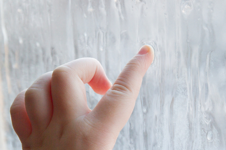 The child's hand draws patterns on the frozen window in winterの写真素材