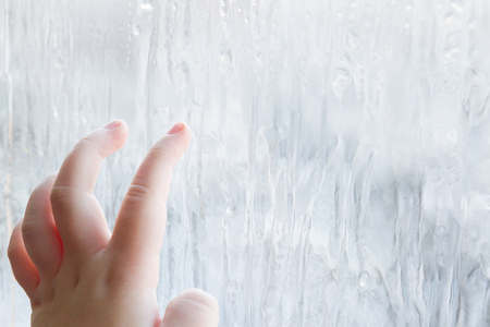 The child's hand draws patterns on the frozen window in winterの写真素材