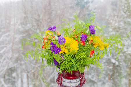 A beautiful vase of spring flowers stands on a window in a snowstormの写真素材