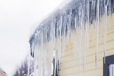 Icicles hang from the roof of a private house in winterの写真素材