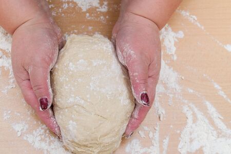 Kneading dough with flour on a wooden table at home