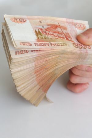 Men's hands hold a large number of banknotes in a pack of five thousand rubles