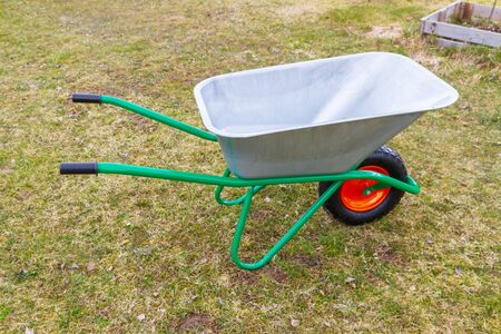 Garden metal wheelbarrow with green reinforced frame on one wheel in the garden
