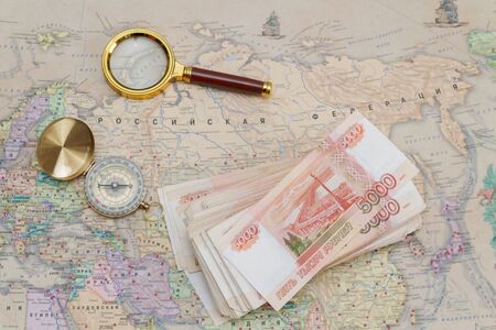A compass with a bundle of big money and a magnifying glass are on the map