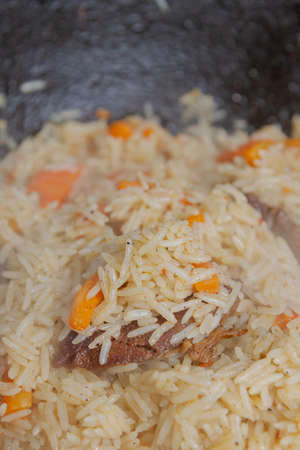 Cooking pilaf in a cauldron on the grill outside in the summer