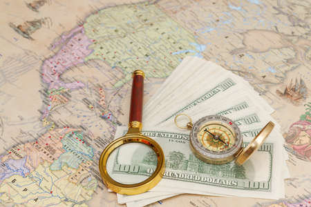 A bundle of american dollars lies with a compass and a magnifying glass on the world mapの写真素材