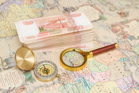A compass with a bundle of big money and a magnifying glass are on the map