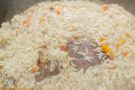 Cooking pilaf in a cauldron on the grill outside in the summer