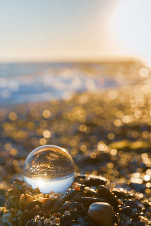 Glass round ball on the beach reflects the sea in summer at sunsetの写真素材