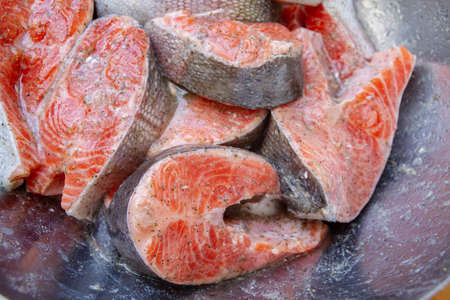 Fresh trout steaks are marinated in a metal bowl before cooking