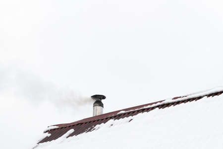 The chimney smokes on the roof of the houseの写真素材