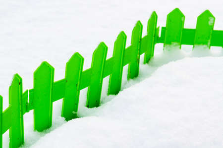 Green plastic fence in the snow in the garden in winterの写真素材