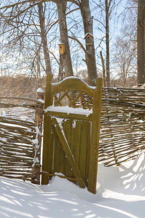 Wooden fence made of sticks with a wooden door in the yard in winterの写真素材