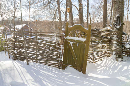 Wooden fence made of sticks with a wooden door in the yard in winterの写真素材