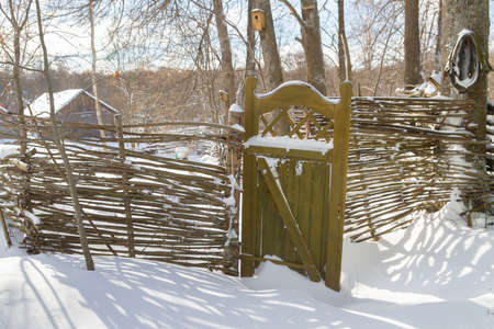 Wooden fence made of sticks with a wooden door in the yard in winterの写真素材