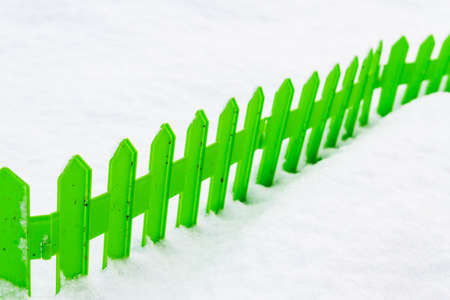 Green plastic fence in the snow in the garden in winterの写真素材