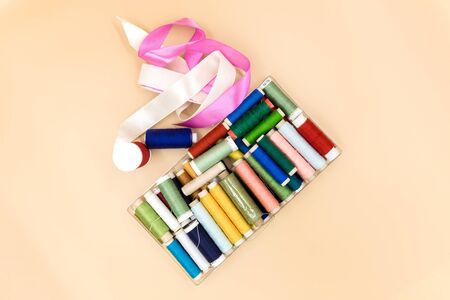 Set threads of different colors and silk ribbons pink on beige background.