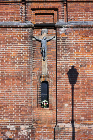 The ancient bronze crucifixion of Christ hangs on a red brick wall background. Sunny dayのeditorial素材