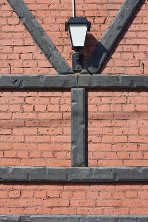 The lantern  hangs on a red  brick wall. Wooden pine logs are laid in the form of Y and H of letters. Concept of secret. Sunny dayの写真素材