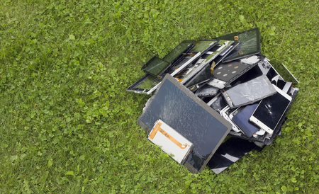 Big heap of the  broken and cracked  cellular telephons and  tablets lie on green lawn grass. Modern...
