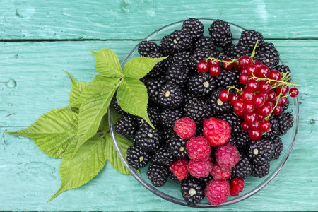 Wild black and red forest  berries lie on green wooden rusric table. Top view background
