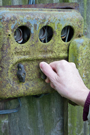 The hand of an elderly woman switches electricity on an old rusty retro rural switchboard. Concept outdoor autumn day photoの写真素材