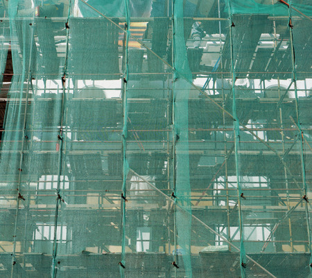 Green plastic mesh on the wall of a renovated urban building protects people from stones. Outdoor...