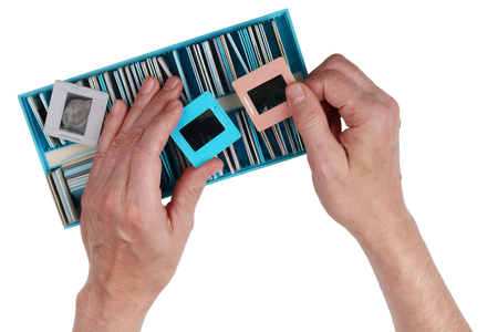 An elderly nostalgic man looks through old film color slides from a family photo archive. Isolated...