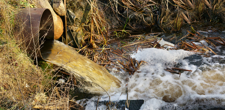 Dirty waste water merges into a clean forest stream. Landscape concept - pollution of the...